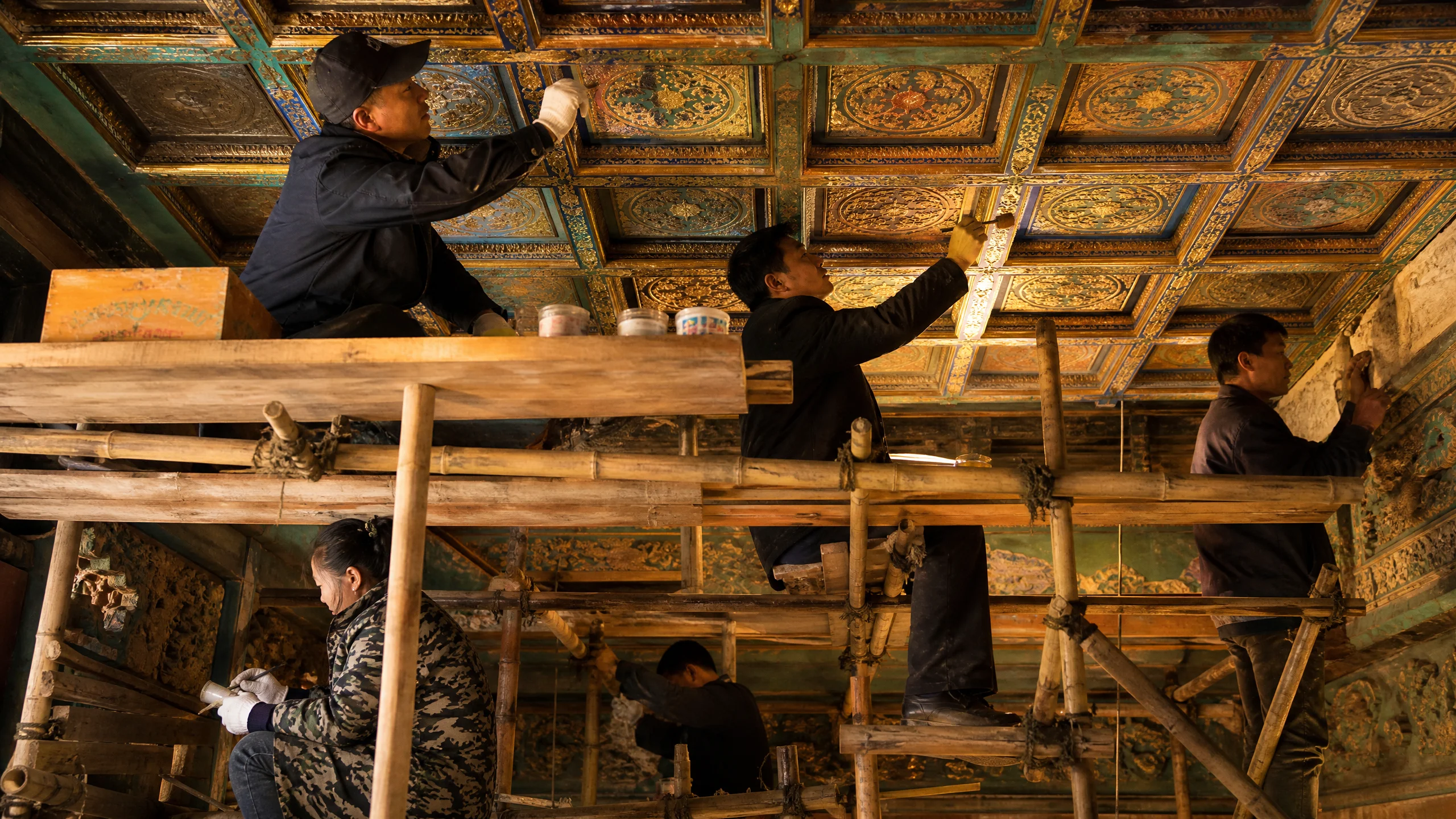 古建筑修复工程现场，工匠在脚手架上修​复藻井彩画